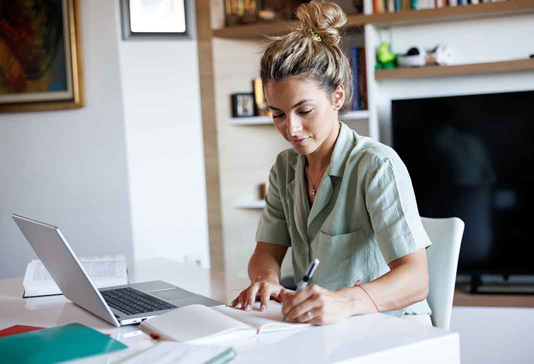 Woman at laptop writing on a pad